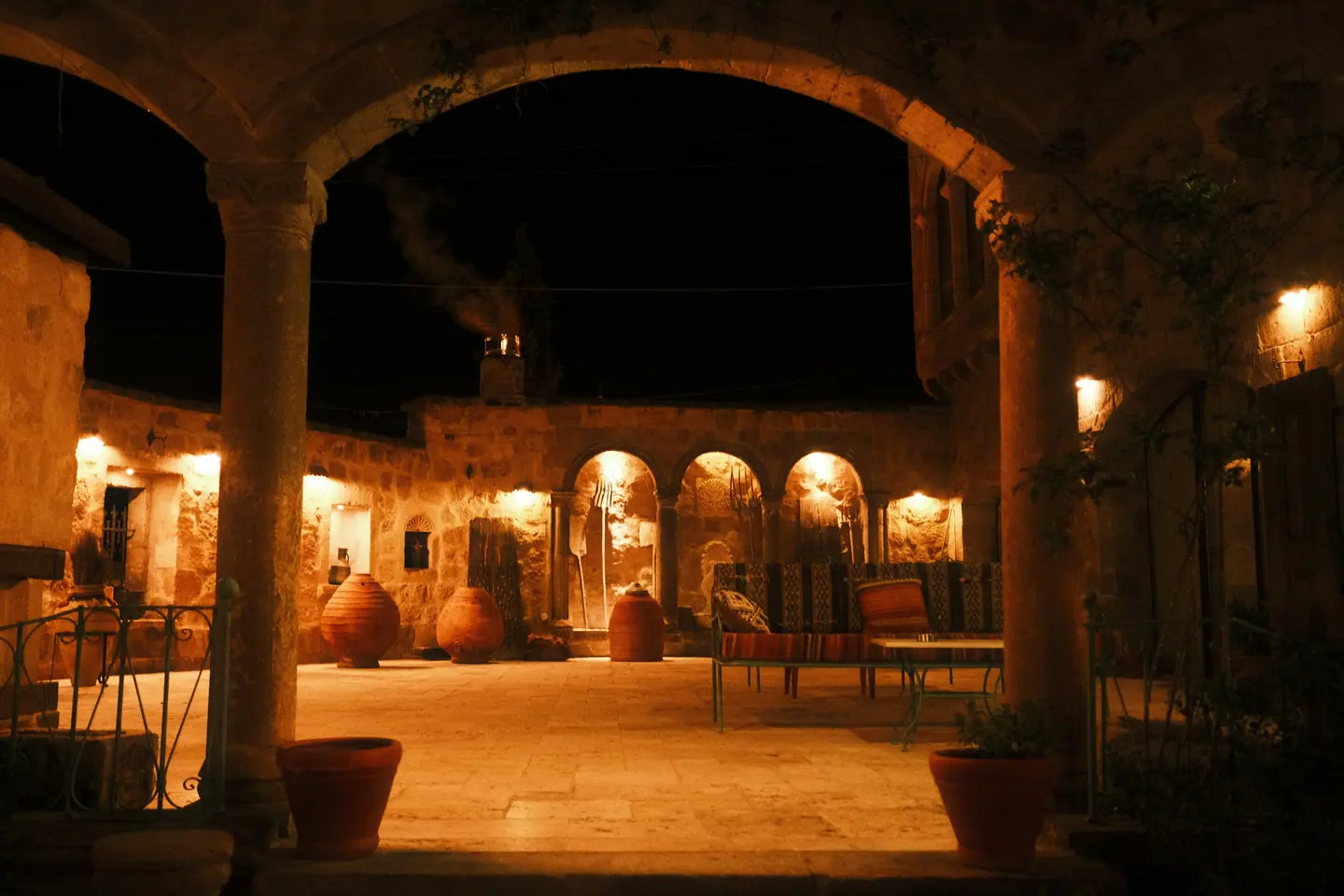 A lamp-lit stone courtyard at night, with pottery and low seating.