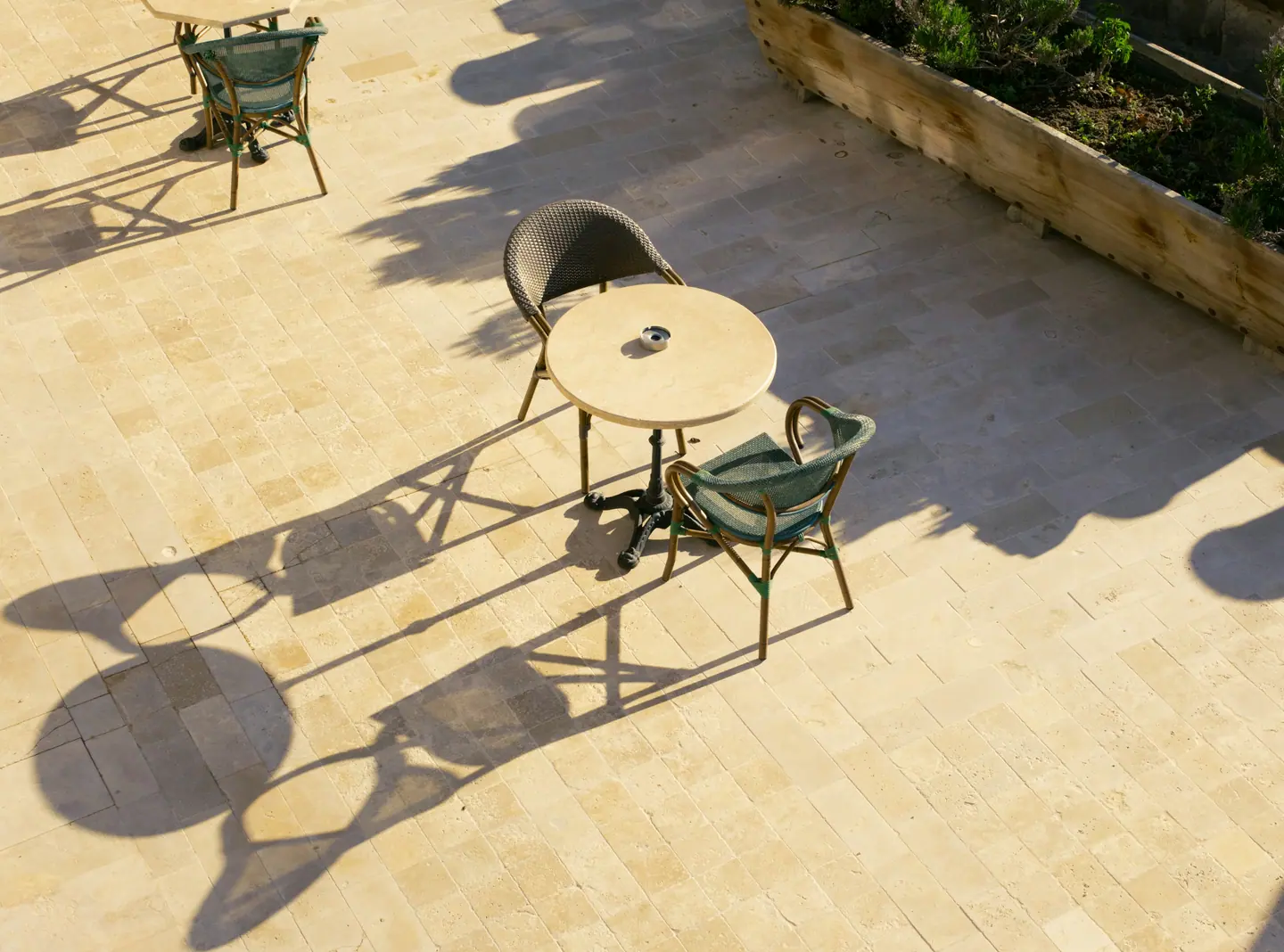 Sunlit travertine paving with a bistro table and long palm shadows.